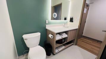 A modern bathroom with a white toilet, a sink with a mirror, and a shower area.