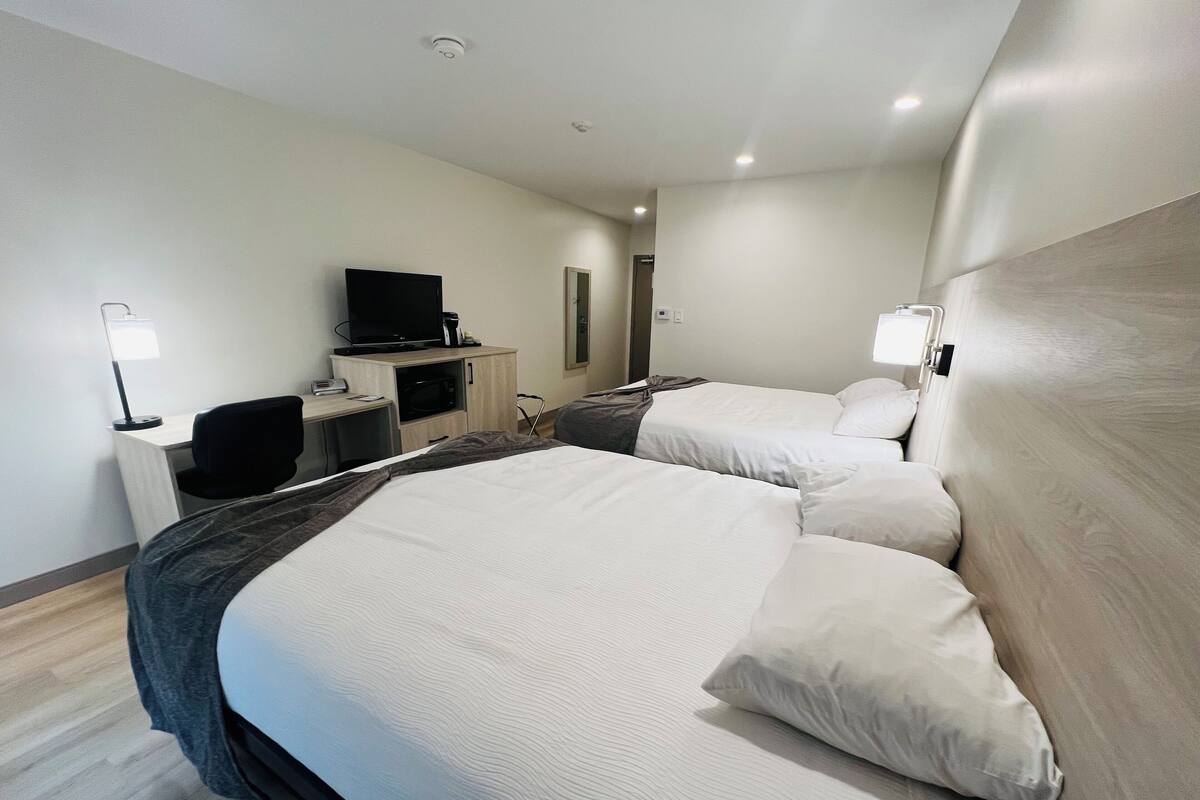 A hotel room with two beds, a desk with a computer, a TV, and a microwave.
