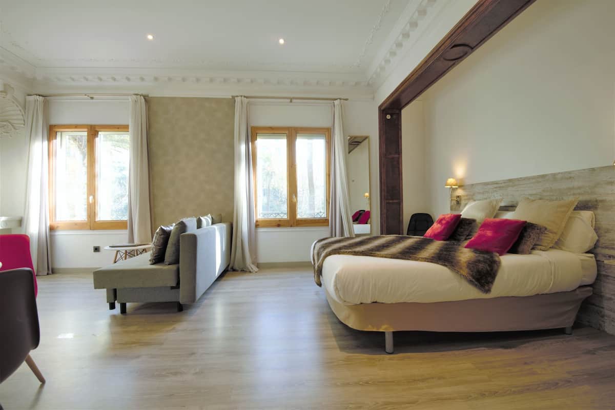 A bedroom with a large bed, a sofa, and two windows with curtains.