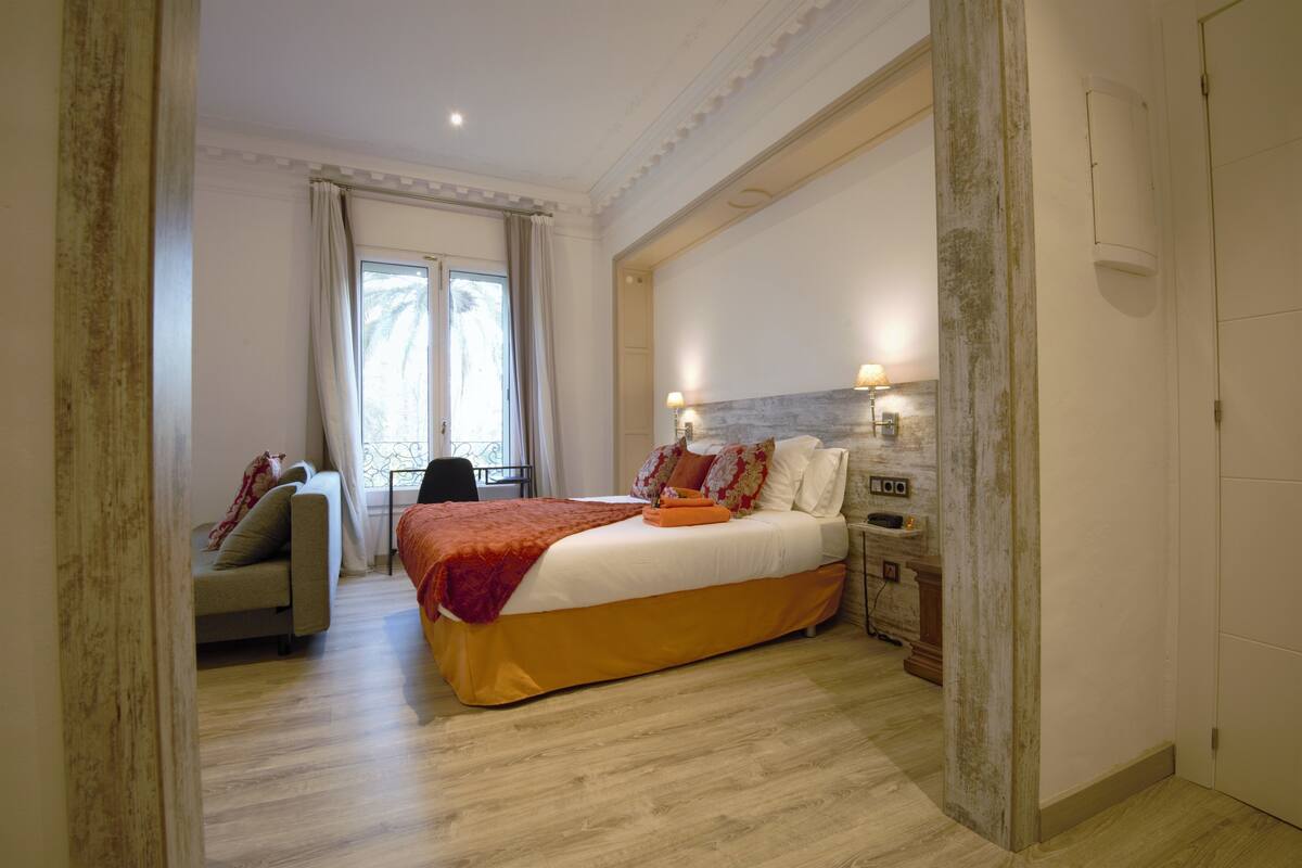 A bedroom with a large bed, a sofa, and a nightstand with lamps.