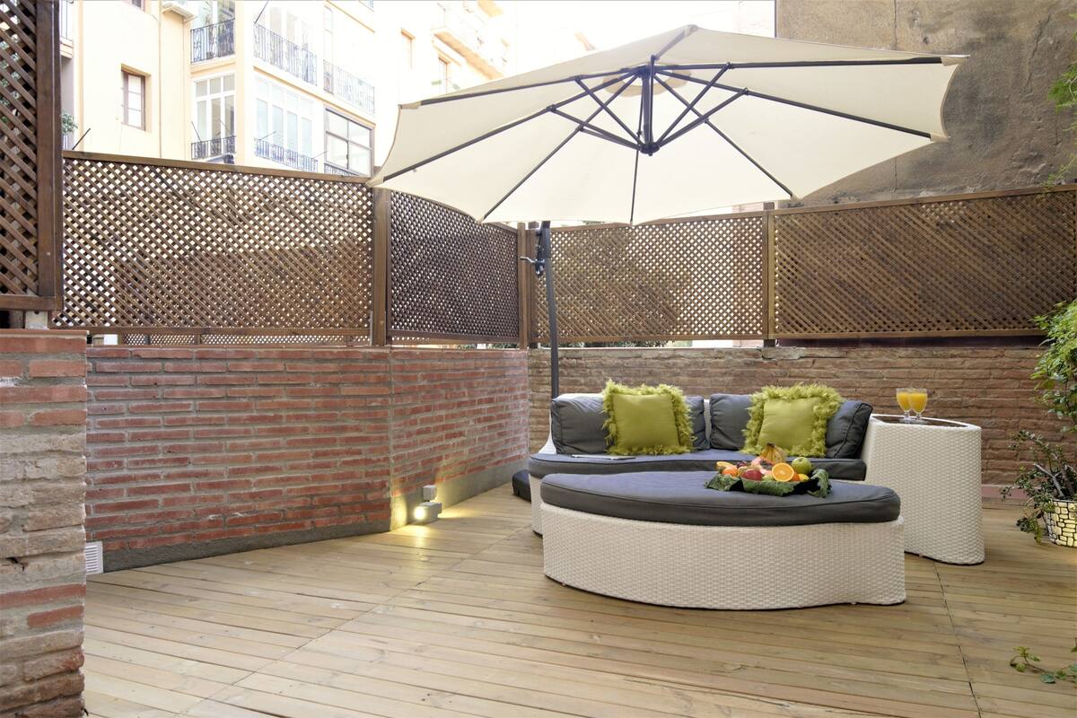 An outdoor seating area with a cushioned sofa, a round table, and a large umbrella.