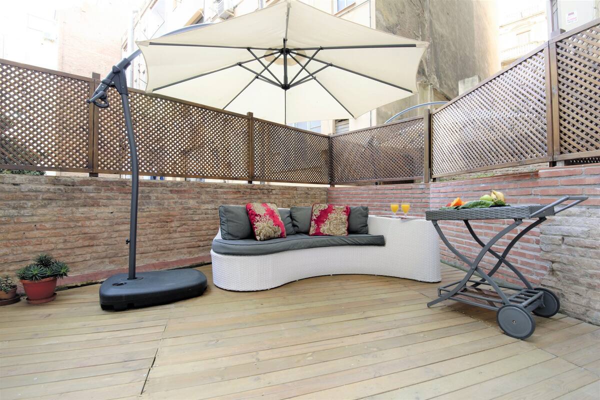 A curved white sofa with red and beige cushions, a large white umbrella, and a wicker cart with fruits.