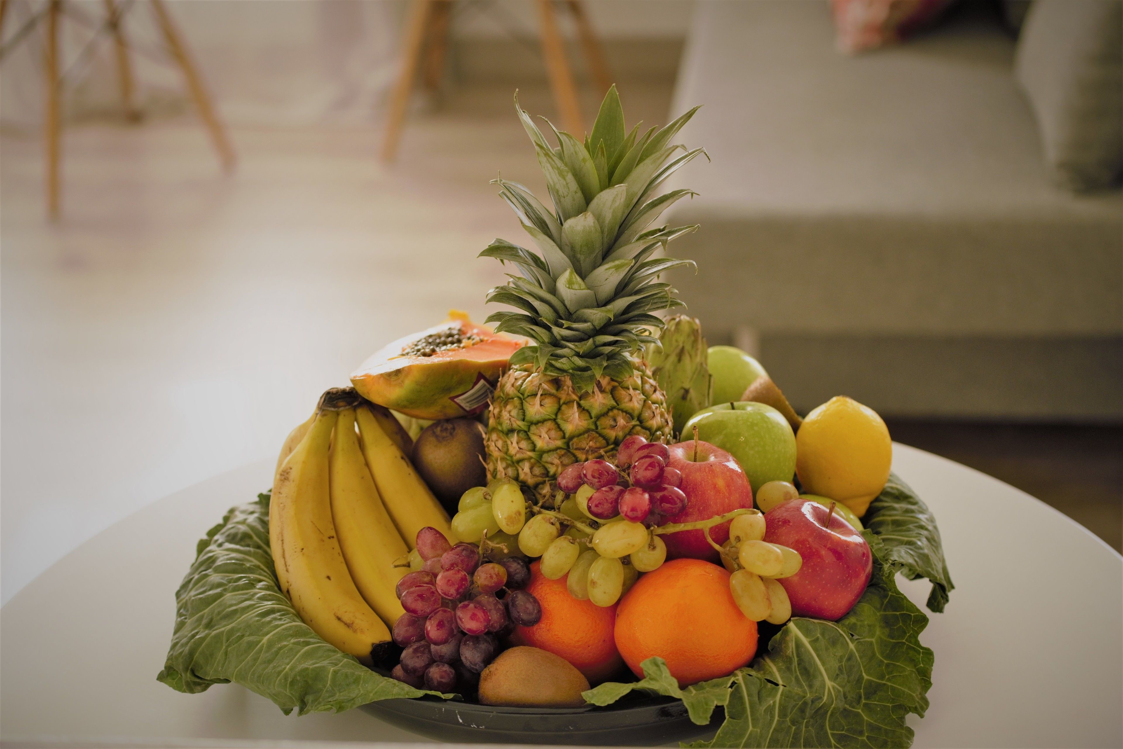 A fruit bowl with bananas, grapes, apples, and a pineapple on a table.