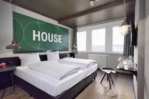 Ett hotellrum med två sängar, en stor skylt med ordet ”HOTEL” på väggen, ett fönster med utsikt och ett litet bord med en stol.