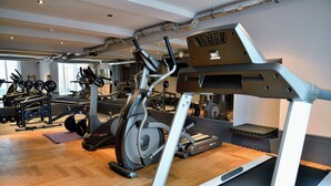 A gym with cardio equipment, weight machines, and a mirrored wall. -  Staytion Urban City Hotel Mannheim (Mannheim)