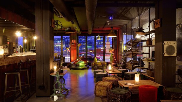A bar area with stools, a counter, and a view of the cityscape through large windows. -  Staytion Urban City Hotel Mannheim (Mannheim)