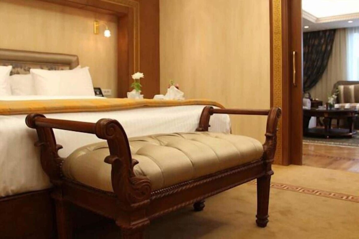 A hotel room with a large bed, a wooden chair, and a small table with a vase of flowers.