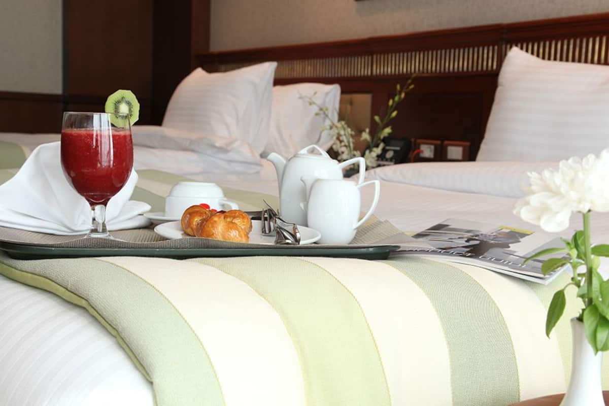 A neatly made bed with a breakfast tray including a glass of red juice, a croissant, a teapot, and a cup.