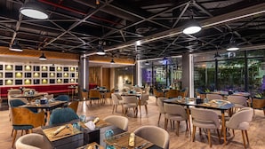 A modern dining area with tables and chairs, large windows, and a high ceiling with exposed beams. - Helnan Landmark Hotel (New Cairo)