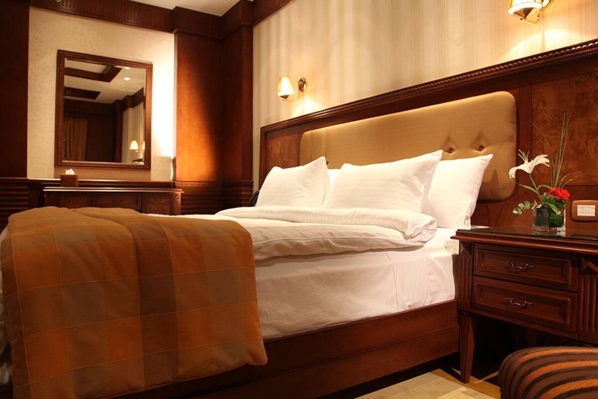 A hotel room with a large bed, a wooden headboard, a nightstand with a lamp, and a mirror on the wall.