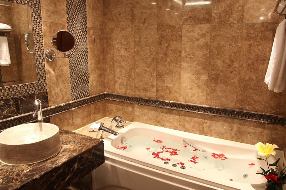 A bathroom with a round sink, a bathtub with rose petals, and a mirror with a round frame.