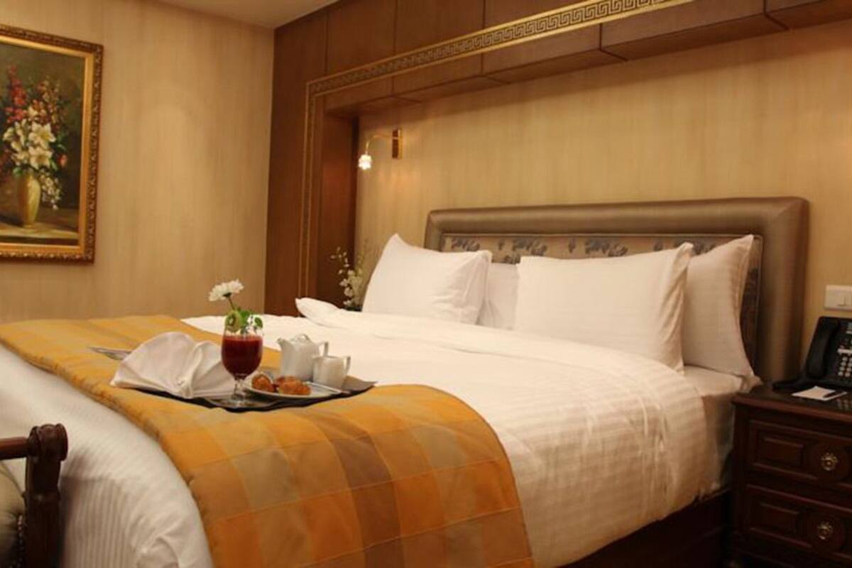 A hotel room with a large bed, a bedside table with a phone, and a painting on the wall.