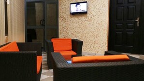 A lobby with wicker furniture, a television mounted on the wall, and a door in the background. - Mint Hotel (Lomé)