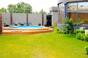 A swimming pool with a tiled deck, surrounded by a grassy lawn and a low wall. - Mint Hotel (Lomé)