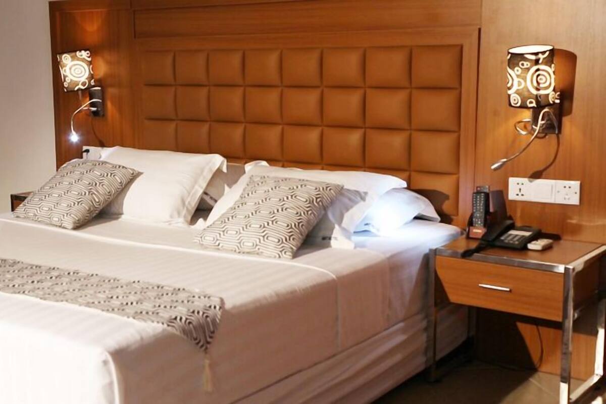 A neatly made bed with patterned pillows, a bedside table with a phone and a lamp, and a wall-mounted light fixture.