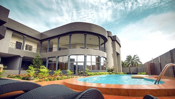 A modern building with a circular pool, outdoor seating, and a well-maintained garden. - Mint Hotel (Lomé)
