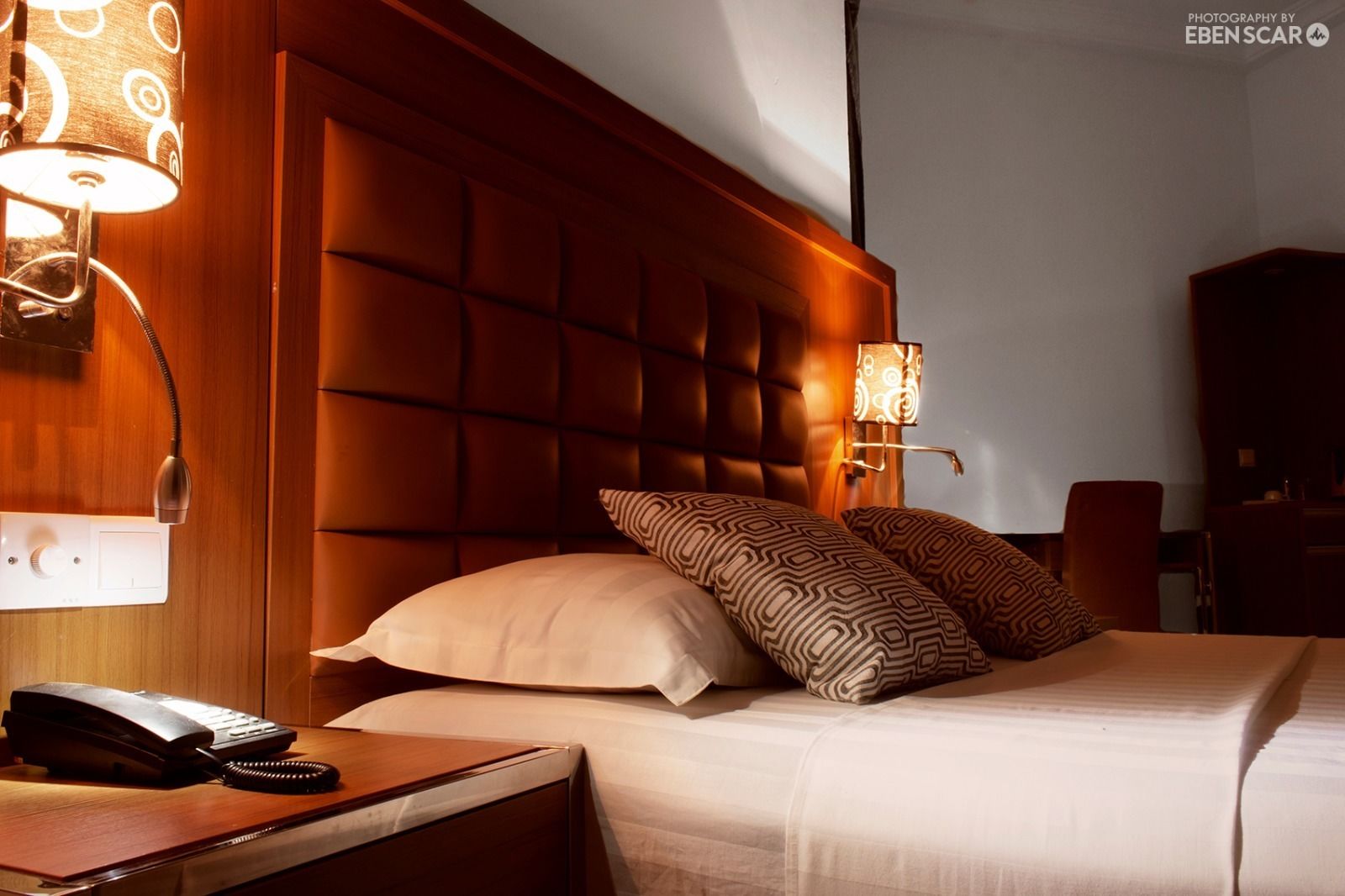 Une chambre d’hôtel avec une tête de lit capitonnée, un téléphone sur la table de chevet et des coussins à motifs.