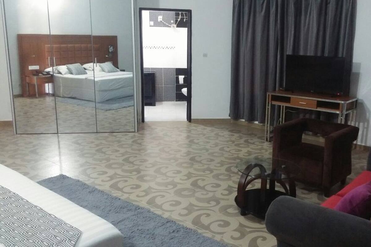 A hotel room with a bed, a TV, a sofa, and a mirror.