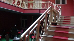Interior de hotel con varios niveles, una escalera, peldaños alfombrados en rojo y un balcón con barandillas blancas.