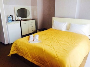 Habitación de hotel con cama, mesita de noche, espejo y pequeño escritorio con una botella de agua y una taza.