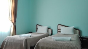 Dos camas individuales con cabeceras y almohadas a juego, una mesita de noche con lámpara, y una ventana con cortinas.