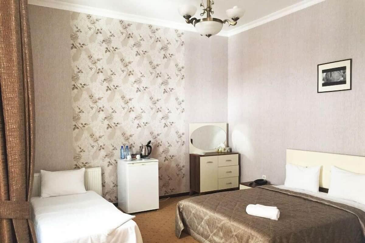 Ein Hotelzimmer mit zwei Betten, einem kleinen Schreibtisch mit Spiegel, einem Kühlschrank und einem Bild an der Wand.