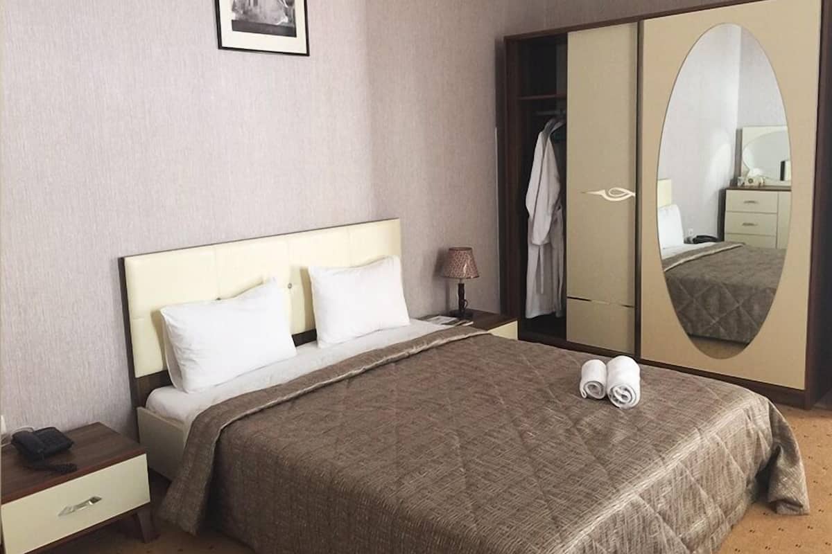 Ein Hotelzimmer mit einem Bett, einem Nachttisch, einer Lampe, einem Kleiderschrank und einem Spiegel.