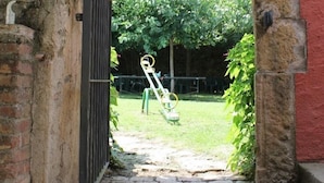 Een inkom met een stenen boog die uitkomt op een grasveld met een hek en een schommelset.
