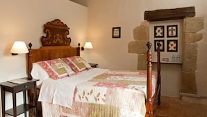 Een slaapkamer met een houten bed, twee nachtkastjes, een stenen muur en ingelijste foto's.