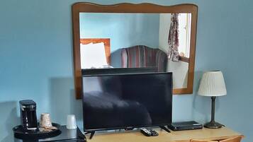 Une chambre d’hôtel de taille modeste, comprenant un bureau en bois, une télévision, un petit réfrigérateur, une chaise et une lampe.