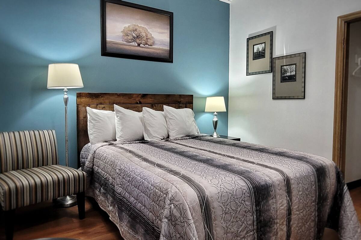 Un dormitorio con una cama grande, dos lámparas de noche, un sillón a rayas y un cuadro en la pared.