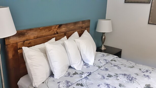 Una cama con cabecera de madera, almohadas blancas y colcha estampada con motivos florales.