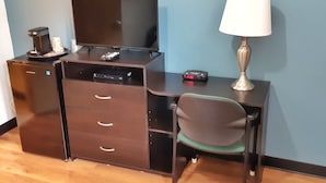 Una habitación pequeña con escritorio, una silla, televisor, cafetera y lámpara.