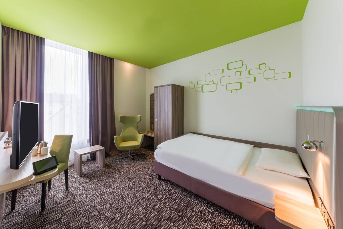 A hotel room with a bed, a desk with a laptop, a chair, and a TV.