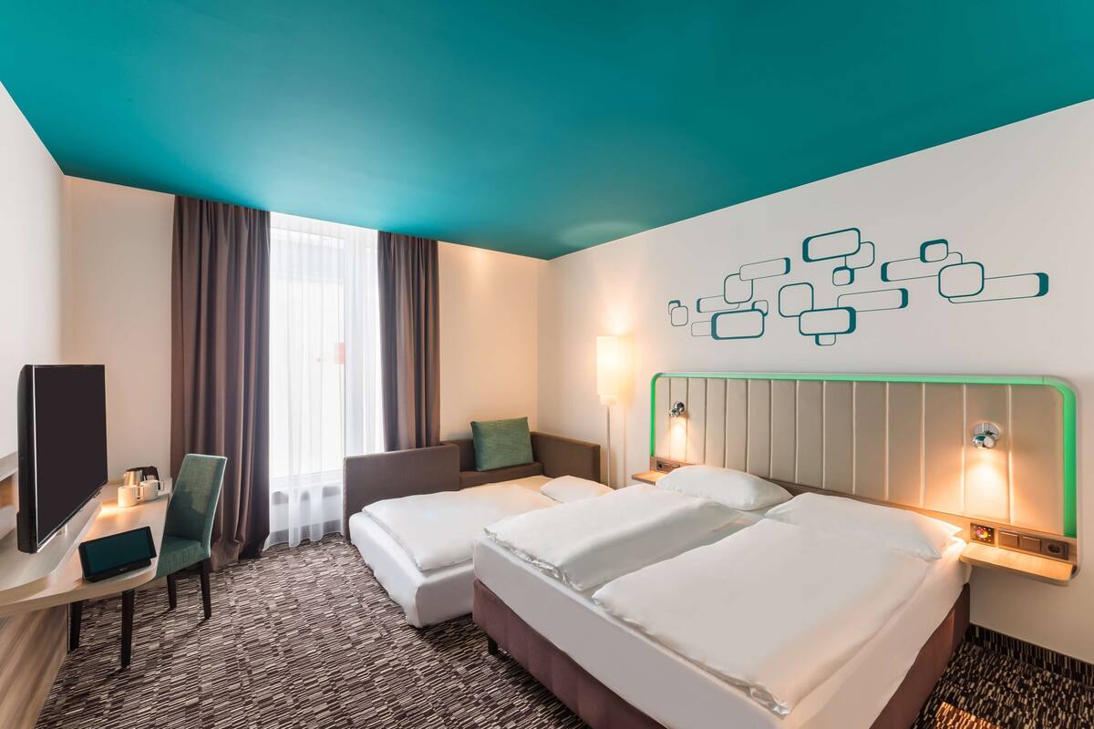 A hotel room with two beds, a desk, a chair, and a TV.