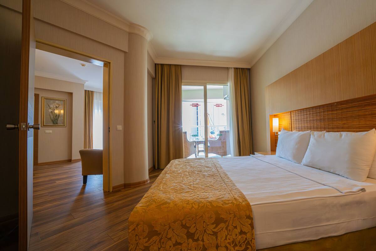 A hotel room with a large bed, wooden headboard, and a view of the outside through a glass door.