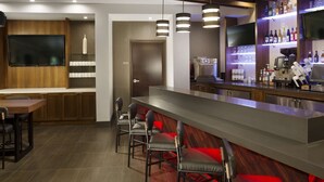 A modern bar area with a long counter, bar stools, a flat-screen TV, and a variety of bottles on shelves. - Hyatt Place Lubbock (Lubbock)