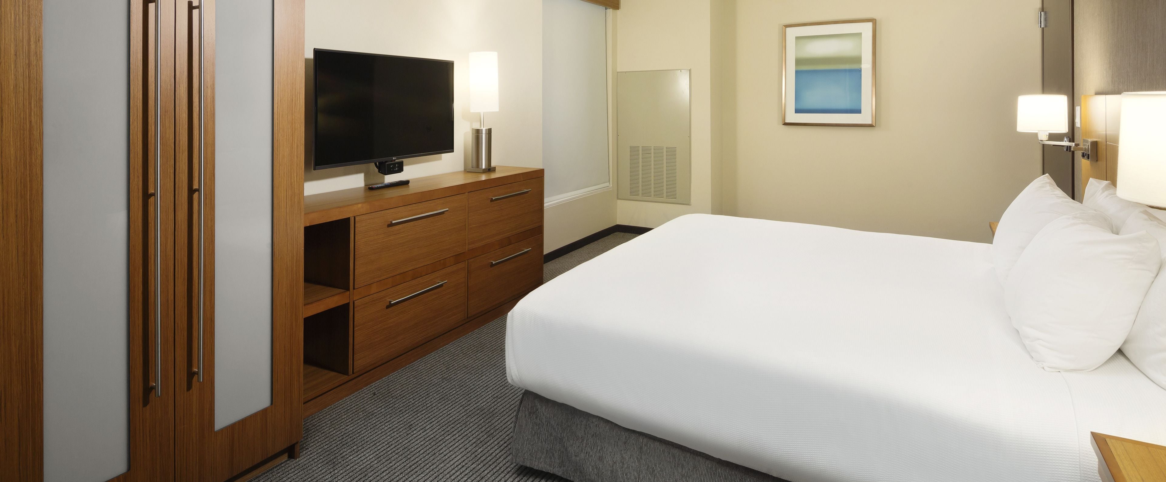 A hotel room with a bed, a TV on a wooden dresser, a mirror, and a painting on the wall.