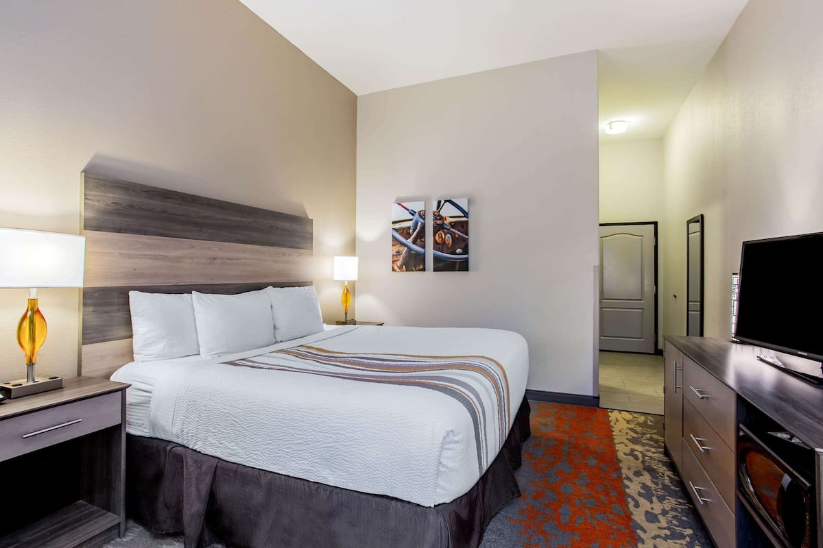 Ein Hotelzimmer mit einem großen Bett, einem Schreibtisch mit Lampe, einem Fernseher und einer Kommode.