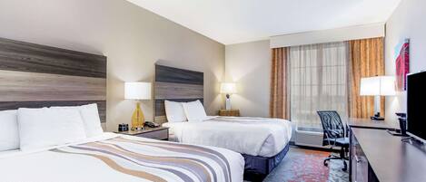 A hotel room with two beds, a desk, a chair, and a TV.