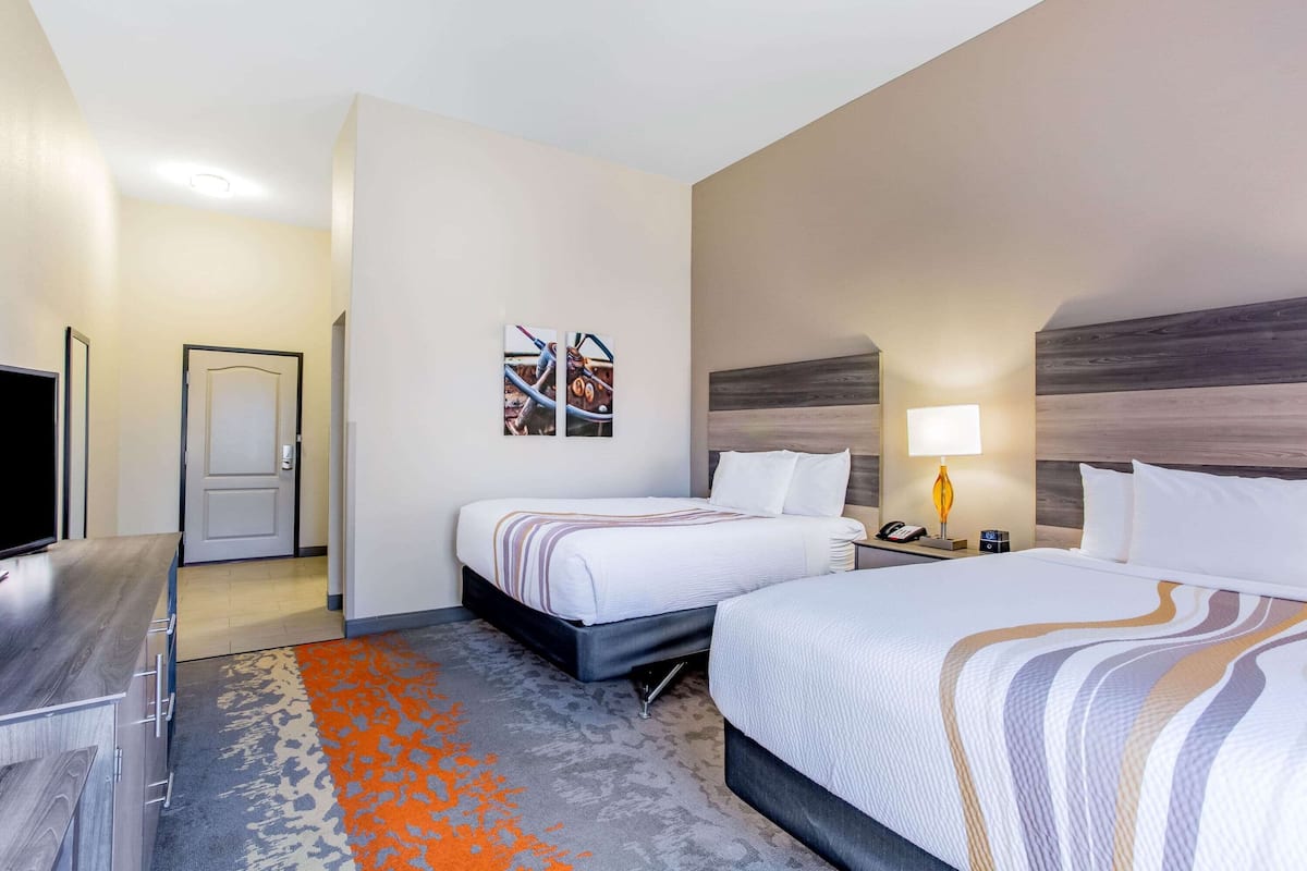 Ein Hotelzimmer mit zwei Betten, einem Schreibtisch, einem Fernseher und Kunstwerken an der Wand.