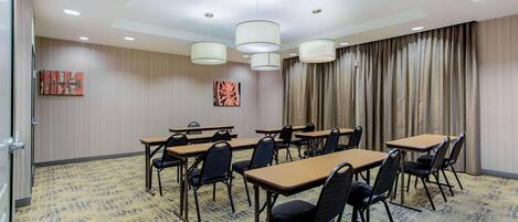 A conference room with tables and chairs, ceiling lights, and curtains.