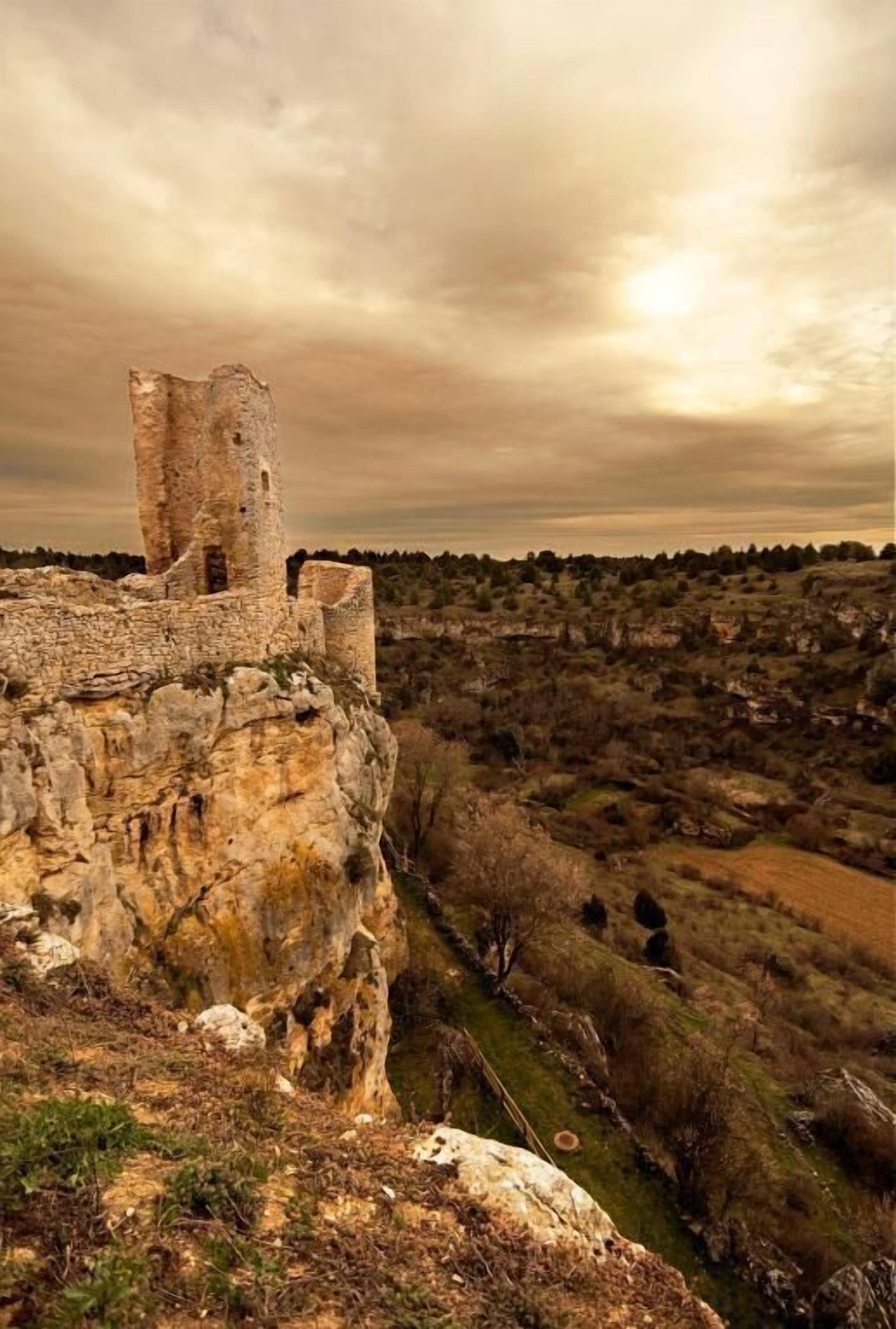 A historical stone structure with a tower, surrounded by a rural landscape.