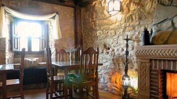 A stone-walled room with a fireplace, wooden furniture, and a window with curtains.