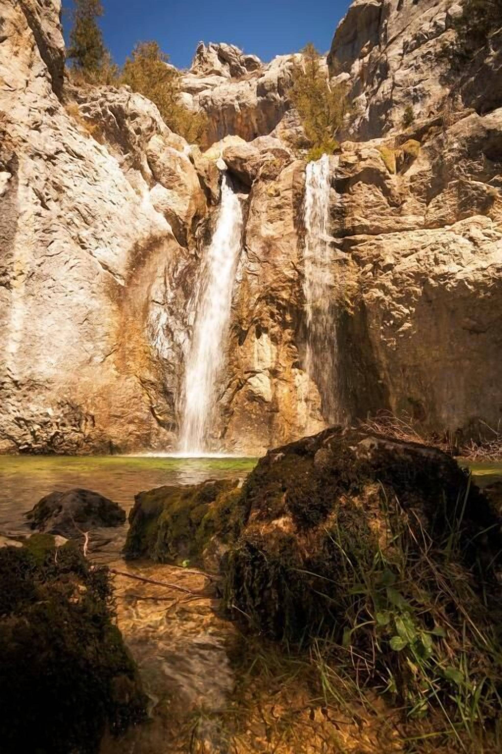 A waterfall cascading into a pool surrounded by rocky terrain.