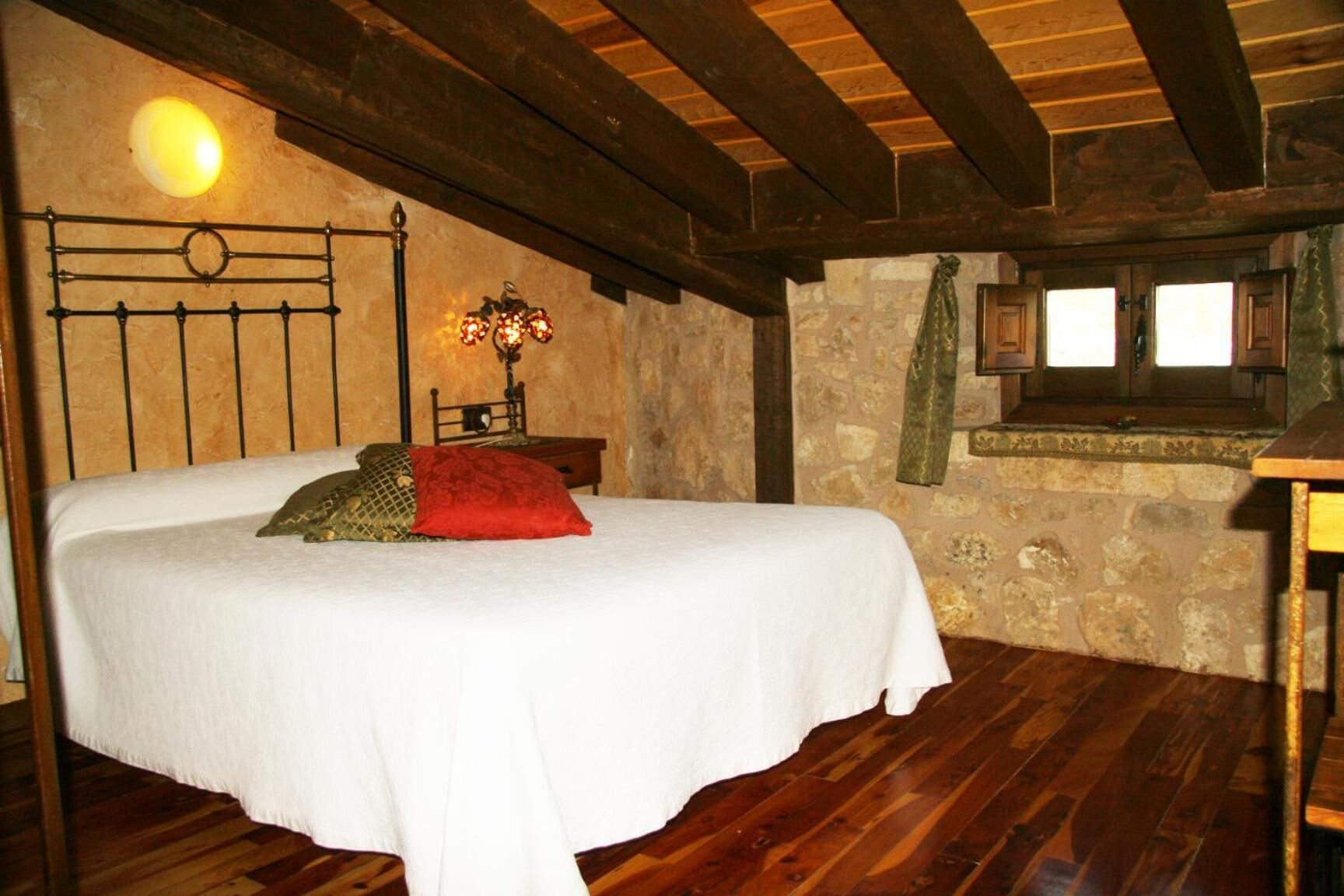 Un dormitorio acogedor con techo de madera, pared de piedra y cama con cubrecama y almohadas blancas.