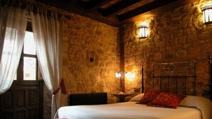 Une chambre aux murs de pierre, avec un lit, une table de chevet, une lampe et une chaise.