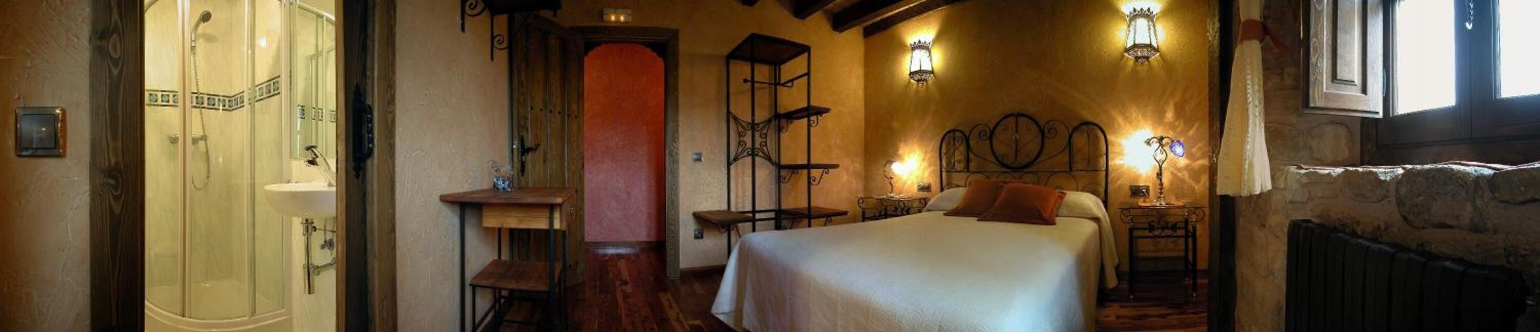 Un dormitorio con cama, mesitas de noche, una silla de madera, una mesita pequeña y un estante en la pared.