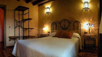 Un dormitorio con cama, mesitas de noche, una silla de madera, una mesita pequeña y un estante en la pared.