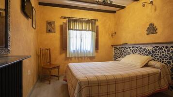 A bedroom with a bed, a chair, a window with curtains, a wall-mounted TV, and a decorative headboard.